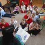 Przedszkolaki siedzą na podłodze i z uwagą słuchają opowiadania czytanego przez nauczyciela