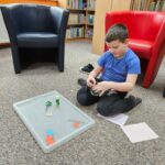 Dziecko siedząc na podłodze wykonuje pracę plastyczną