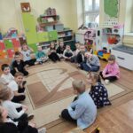 Dzieci siedzą na ziemi i z uwagą słuchają opowiadania