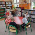 Uczestnicy zajęć siedzą przy czerwonym stole i aktywnie uczestniczą w zajęciach