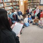 Dzieci siedzą na ziemi i z uwagą słuchają czytanego przez panią opowiadania