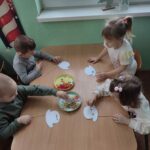 Dzieci siedzą przy stoliku i wykonują pracę plastyczną