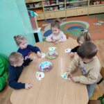 Dzieci siedzą przy stoliku i wykonują pracę plastyczną