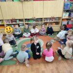 Dzieci siedzą na ziemi i z uwagą słuchają opowiadania