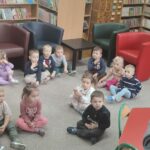Dzieci siedzą na ziemi i z uwagą słuchają czytanego przez panią opowiadania