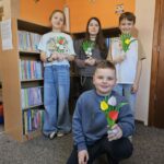 "Moliki" stoją na tle bibliotecznych regałów z książkami i prezentują wykonane przez siebie prace