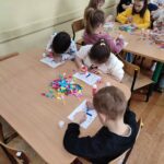 Dzieci przy stoliku wykonują pracę plastyczną