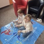 Ddziewczynki siedzą na ziemi i wykonują pracę plastyczną