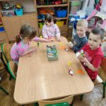 Dzieci przy stoliku wykonują pracę plastyczną