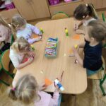 Dzieci przy stoliku wykonują pracę plastyczną