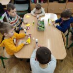 Dzieci przy stoliku wykonują pracę plastyczną