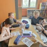 Dzieci przy stoliku w bibliotece wykonują pracę plastyczną.
