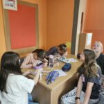 Dzieci przy stoliku w bibliotece wykonują pracę plastyczną.