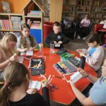 Dzieci przy stoliku w bibliotece wykonują pracę plastyczną.