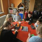 Dzieci przy stoliku w bibliotece wykonują pracę plastyczną.