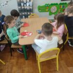 Dzieci przy stoliku w bibliotece wykonują pracę plastyczną.