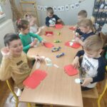 Dzieci przy stoliku w bibliotece wykonują pracę plastyczną.