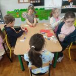 Dzieci przy stoliku w bibliotece wykonują pracę plastyczną.