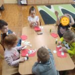 Dzieci przy stoliku w bibliotece wykonują pracę plastyczną.