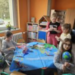 Dzieci przy stoliku w bibliotece wykonują pracę plastyczną.