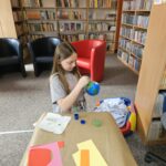 Dzieci przy stoliku w bibliotece wykonują pracę plastyczną.