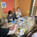 Dzieci przy stoliku w bibliotece wykonują pracę plastyczną.