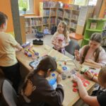 Dzieci przy stoliku w bibliotece wykonują pracę plastyczną.