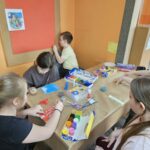 Dzieci przy stoliku w bibliotece wykonują pracę plastyczną.