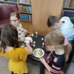 Dzieci przy stoliku w bibliotece wykonują pracę plastyczną