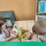 Dzieci przy stoliku w bibliotece wykonują pracę plastyczną