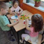 Dzieci przy stoliku w bibliotece wykonują pracę plastyczną