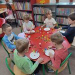 Dzieci przy stoliku w bibliotece wykonują pracę plastyczną
