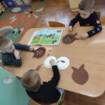 Dzieci siedzą przy stole i wykonują pracę plastyczną.