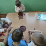 Dzieci siedzą przy stole i wykonują pracę plastyczną.