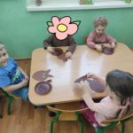 Dzieci siedzą przy stole i wykonują pracę plastyczną.