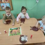 Dzieci siedzą przy stole i wykonują pracę plastyczną.