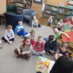 Dzieci siedzą na ziemi i z uwagą słuchają opowiadania