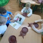 Dzieci siedzą przy stole i wykonują pracę plastyczną.