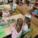Dzieci przy stoliku w bibliotece wykonują pracę plastyczną
