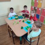 Dzieci siedzą przy stole i wykonują pracę plastyczną
