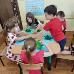 Dzieci siedzą przy stole i wykonują pracę plastyczną