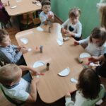 Dzieci przy stoliku wykonują pracę plastyczną