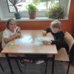 Dzieci przy stoliku z pamiątkowymi dyplomami i delektują się przygotowanymi specjalnie dla nich babeczkami.