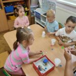 Dzieci przy stoliku wykonują pracę plastyczną