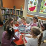 Uczestnicy spotkania przy stoliku wykonują pracę plastyczną