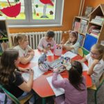 Uczestnicy spotkania przy stoliku wykonują pracę plastyczną